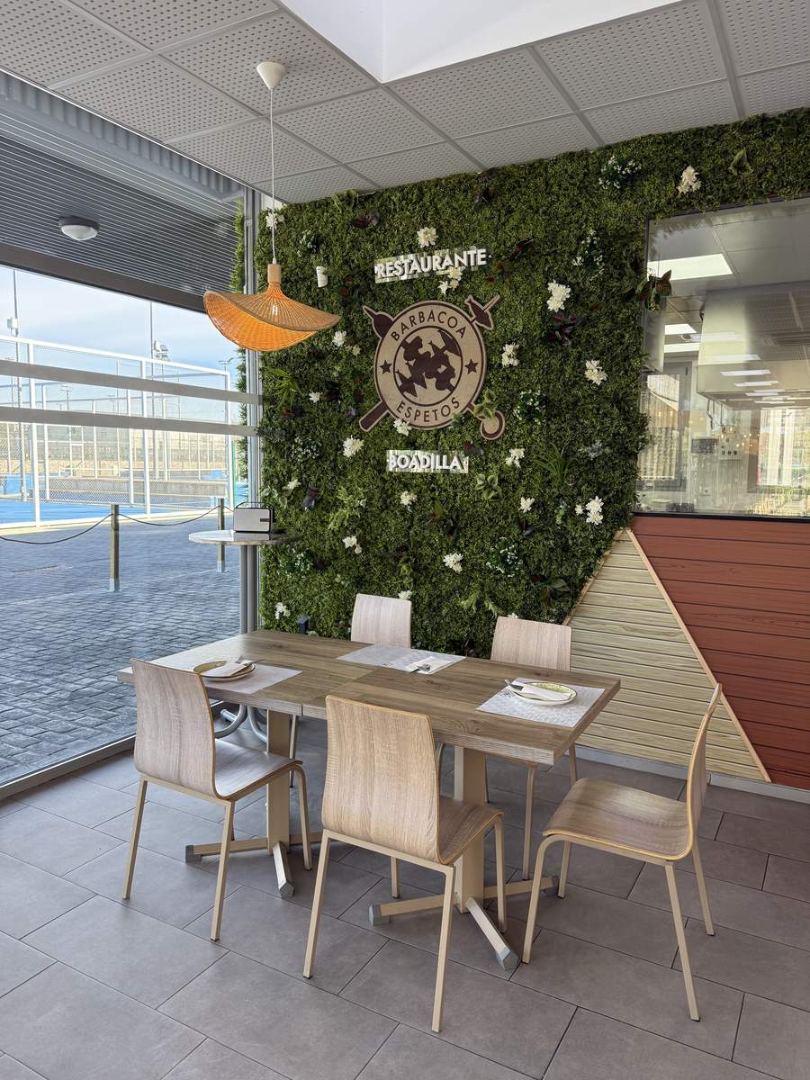 Rincón interior con el logotipo del restaurante sobre un muro vegetal